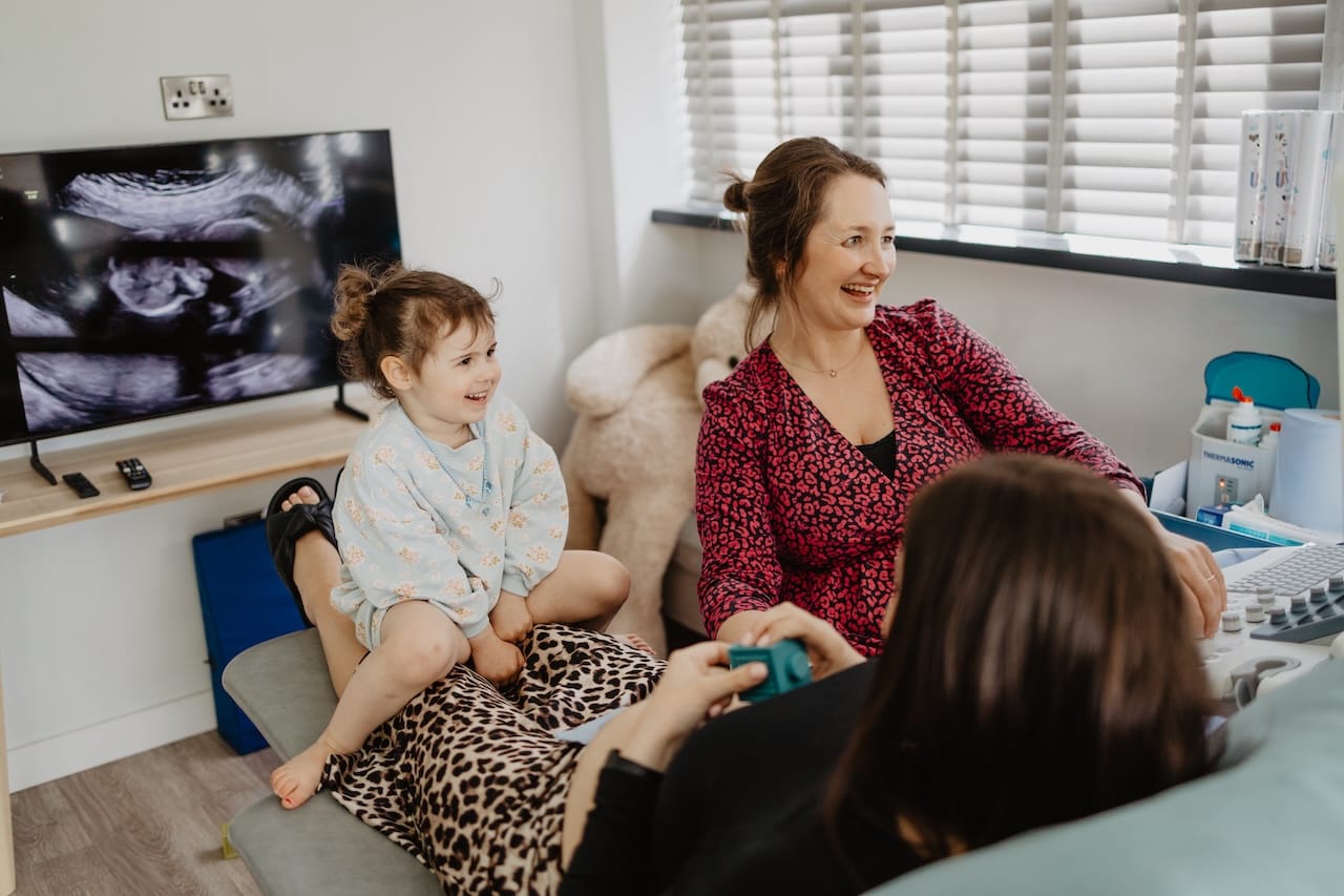 Maria performing a parent's gender scan in Barnstaple with her daughter smiling on her lap.